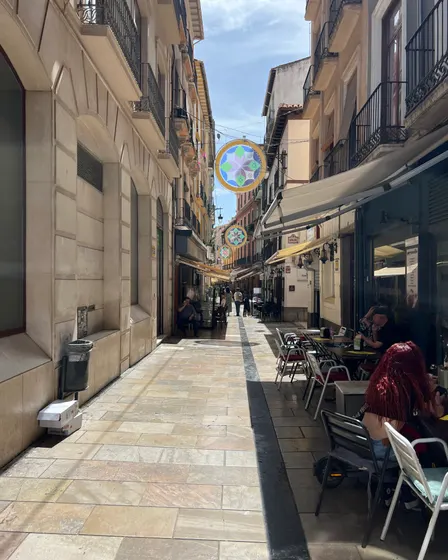 Calle Navas vista a lo largo, con las mesas de las terrazas a la derecha, la acera de piedra y las guirnaldas de colores colgadas entre los balcones.